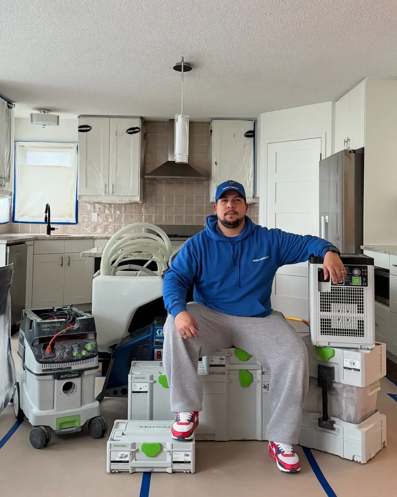 A Chamos Painting team member on-site in a Calgary kitchen with professional dust-extraction and prep equipment for cabinet refinishing
