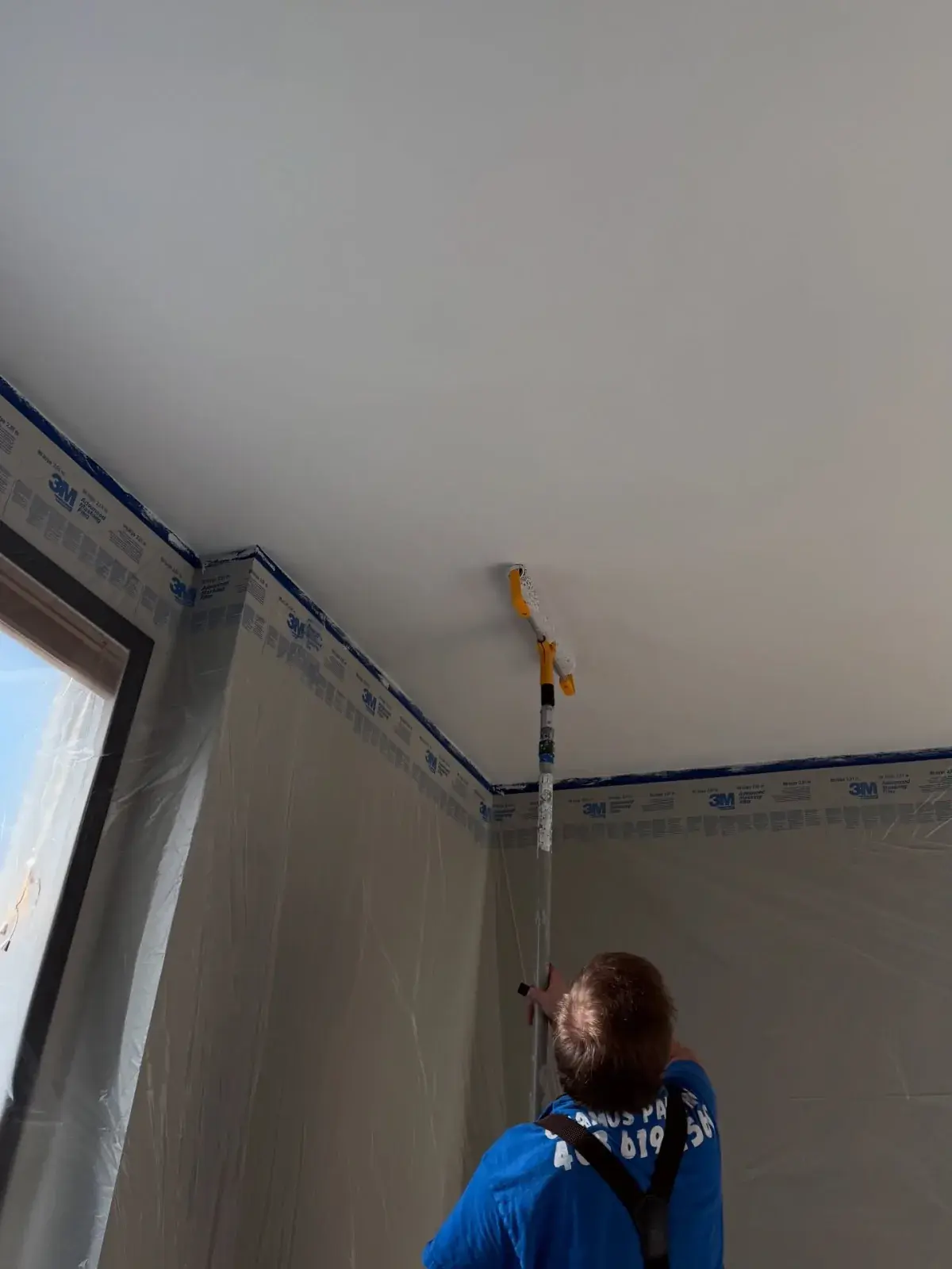 A Chamos Painting painter rolling a fresh coat onto a masked-off ceiling during an interior painting job in Calgary